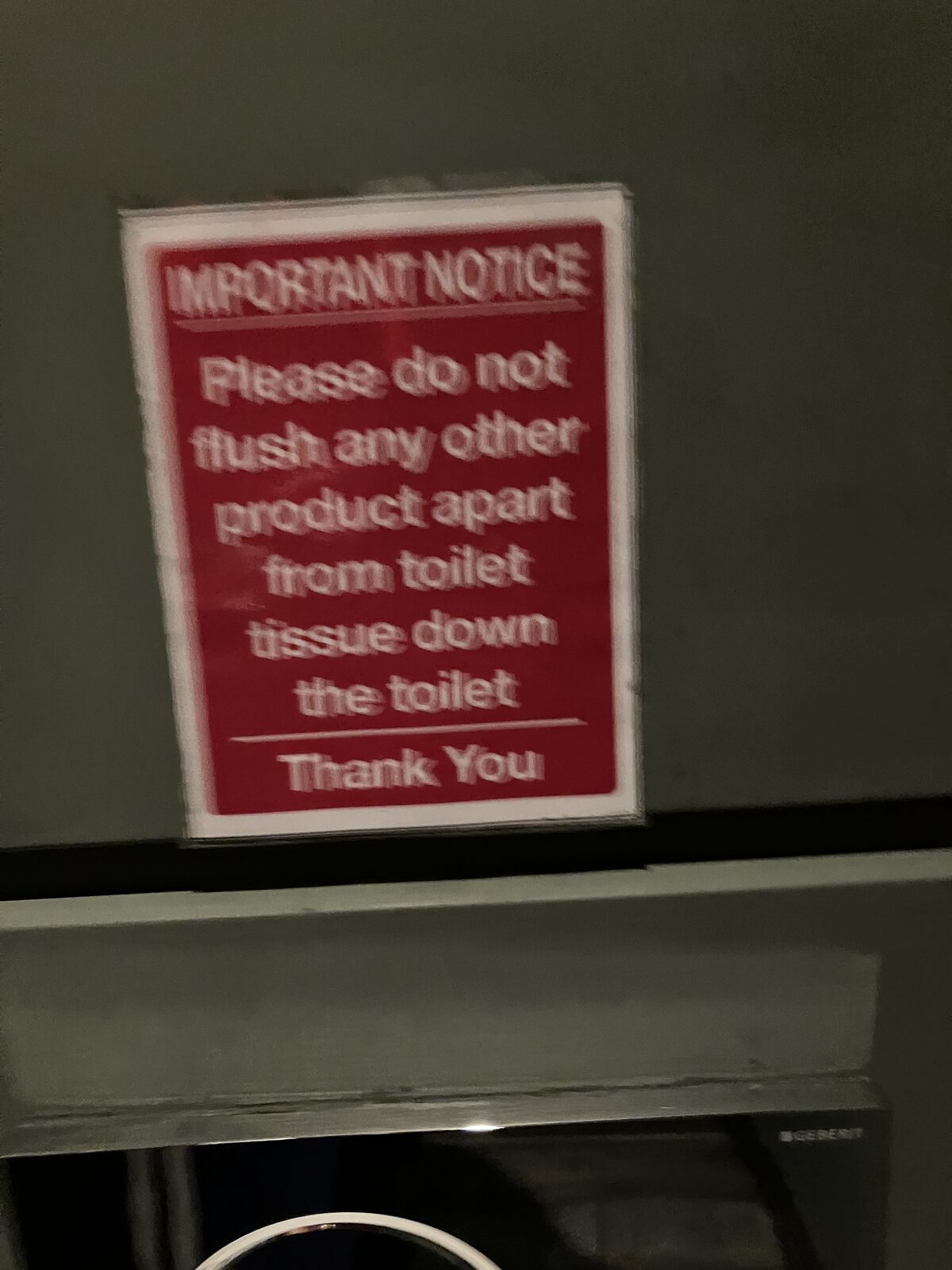 A red sign mounted high on a dark wall stating that nothing except toilet tissue should be flushed down the toilet.